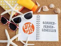 Ein aufgeschlagenes Notizbuch mit dem Logo "Lesen was geht" und "Sommerferien-Leseclub" liegt im Sand.