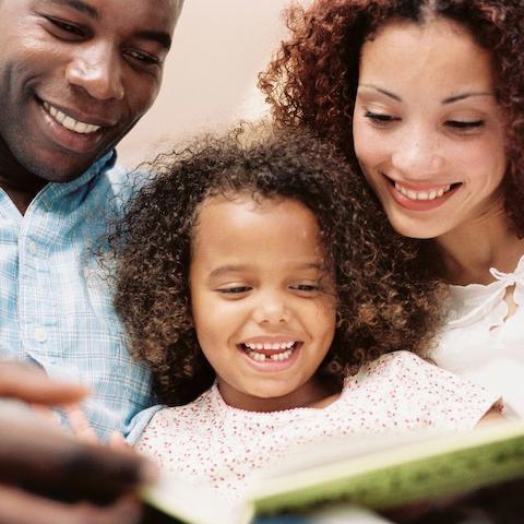 Vater, Mutter und Kind schauen ein Buch an.