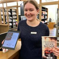 Eine Praktikantin in der Stadtbibliothek hält in der rechten Hand ein iPad und in der linken Hand ein Buch.