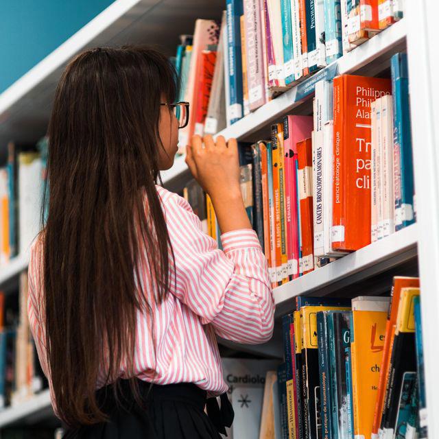 Eine Schülerin steht am Regal und sucht nach einem Buch.