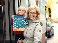 Eine Mutter mit Tochter nach der Ausleihe eines Bilderbuches vor dem Fahrzeug der Fahrbibliothek.