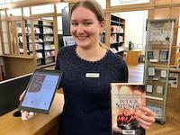 Eine Praktikantin in der Stadtbibliothek hält in der rechten Hand ein iPad und in der linken Hand ein Buch.