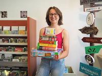 Eine junge Frau hält eine Stapel mit Spielen, Büchern, einer DVD, einer CD und einer Tonie-Figur.