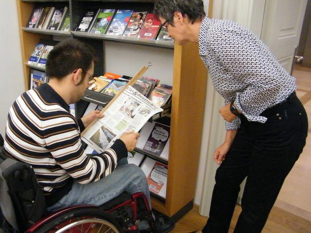 Rollstuhlfahrer in Stadtbibliothek Erlangen im Gespräch mit Mitarbeiterin